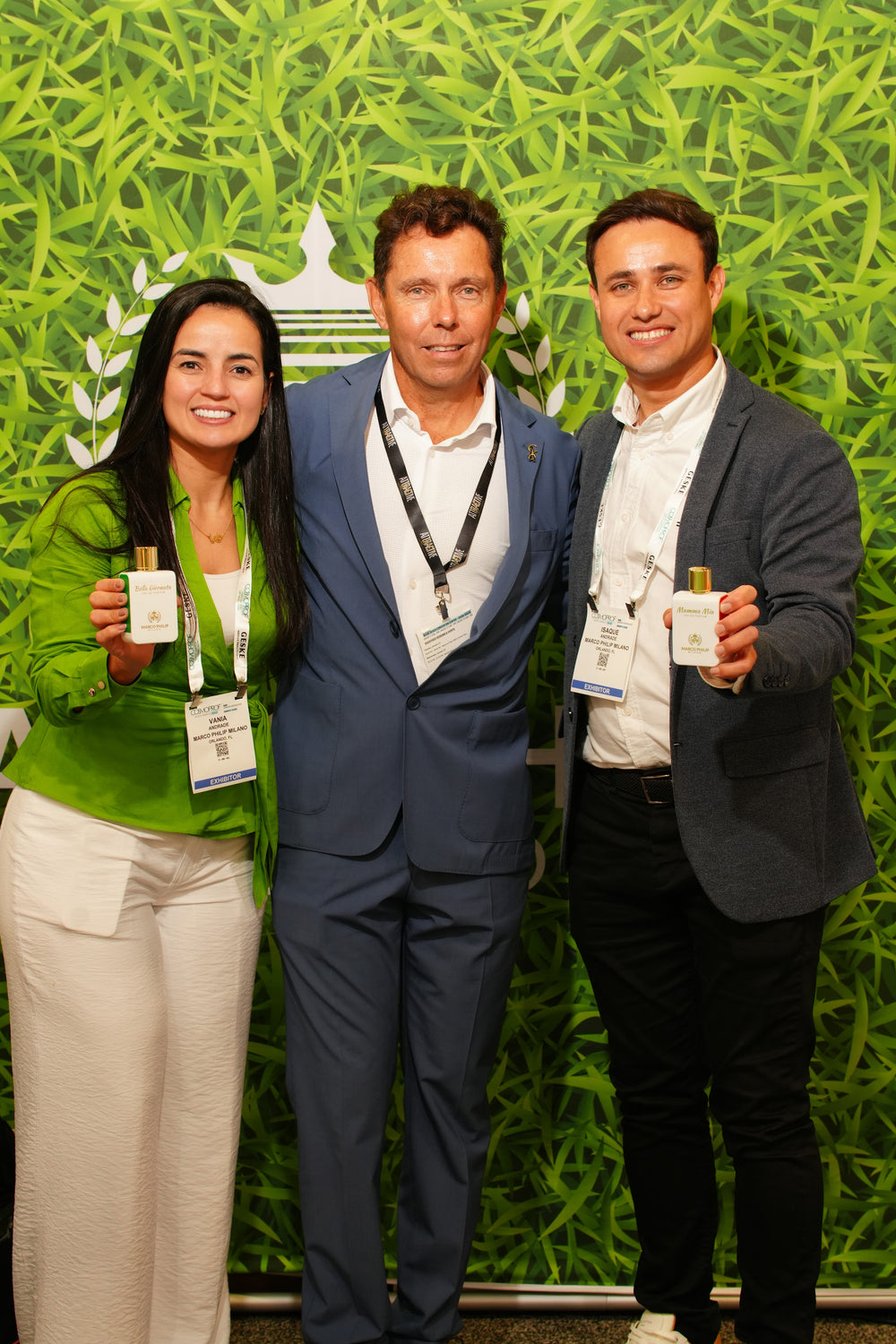 Three people holding Marco Philip Milano bottles in front of the crest wall